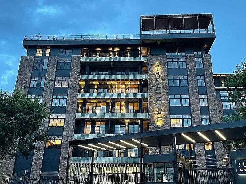 Modern multi-story apartment building facade featuring stone cladding, private balconies, and a secure gated entrance with a guard house.