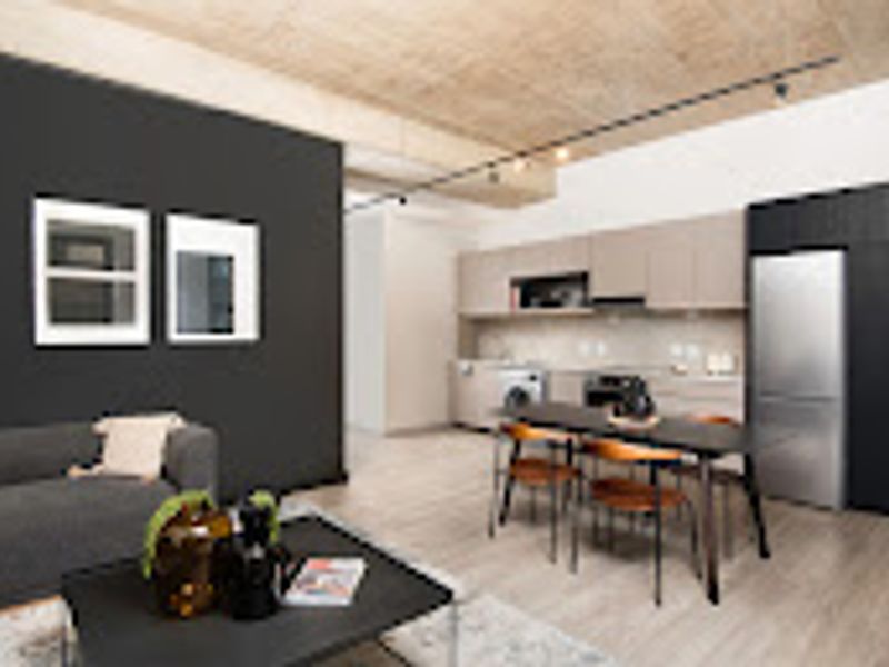 Modern open-plan living area featuring an exposed concrete ceiling, track lighting, and a sleek kitchen with integrated appliances and contemporary cabinetry.