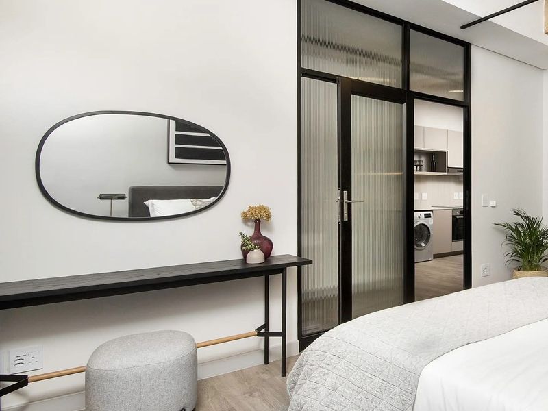 Modern bedroom featuring a stylish fluted glass partition, exposed concrete ceiling, and high-quality laminate flooring, with a view into the adjacent laundry area.