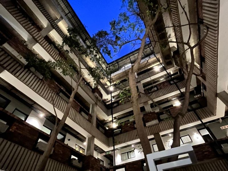 A striking view looking up through the central atrium of an apartment complex, featuring multi-level balconies, exposed brick architecture, and mature trees.