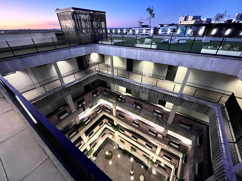 An elevated aerial view of a modern apartment complex featuring a central atrium, open-air walkways, and a rooftop terrace at dusk.