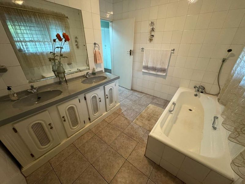 A functional bathroom featuring a double vanity with built-in cabinetry, tiled walls and flooring, and a standard bathtub.