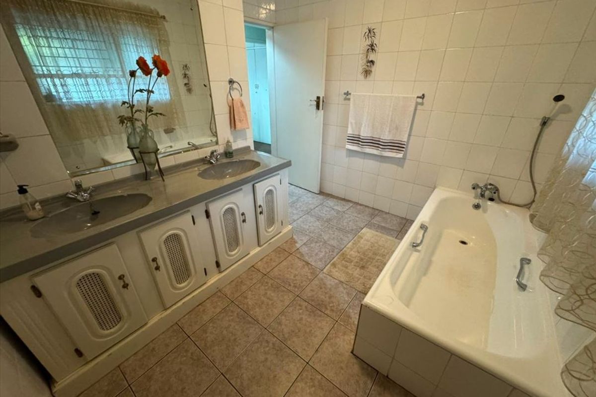 A functional bathroom featuring a double vanity with built-in cabinetry, tiled walls and flooring, and a standard bathtub.
