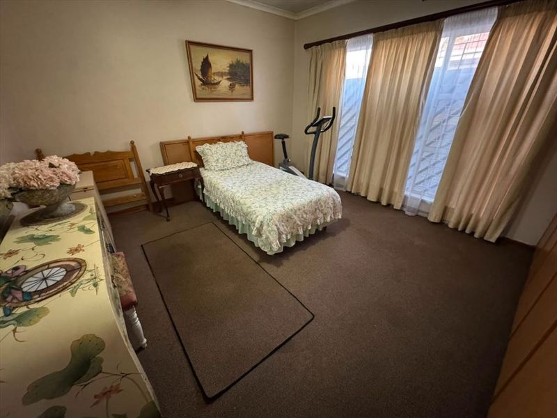 A carpeted bedroom featuring built-in cupboards and large windows with curtain rails, offering a functional and well-lit living space.