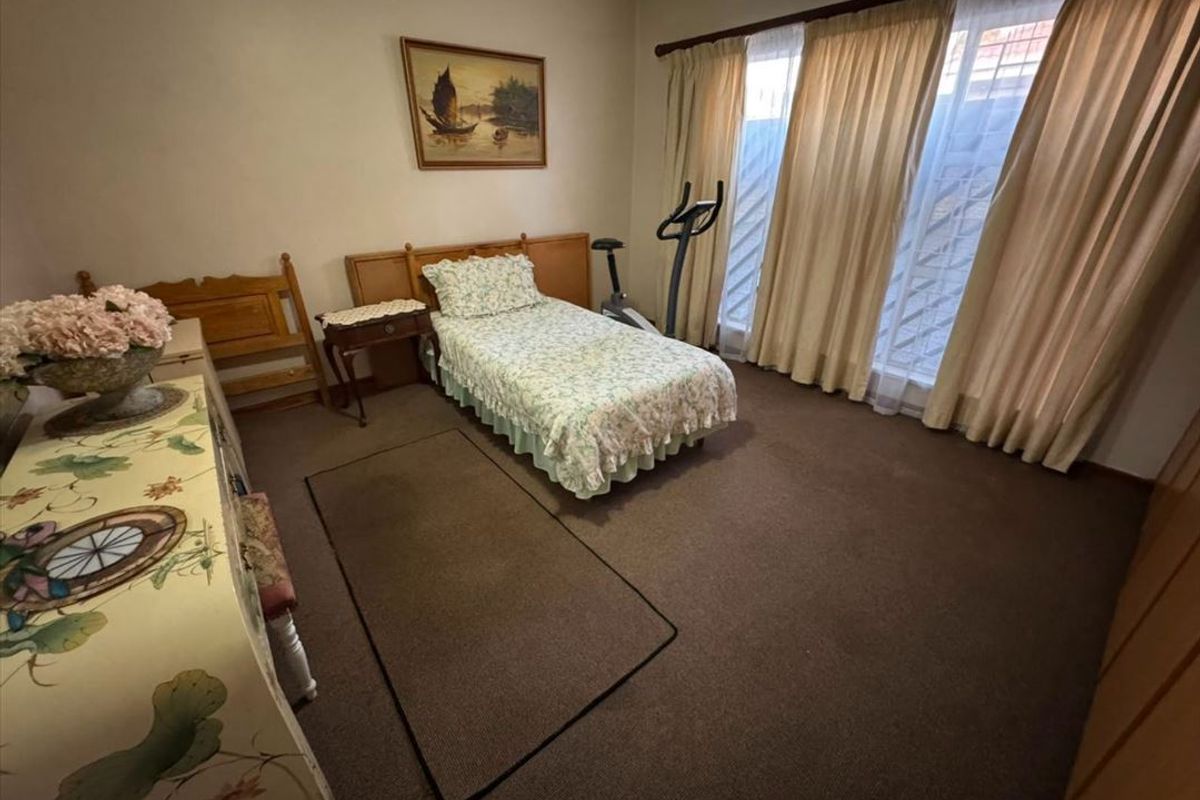 A carpeted bedroom featuring built-in cupboards and large windows with curtain rails, offering a functional and well-lit living space.