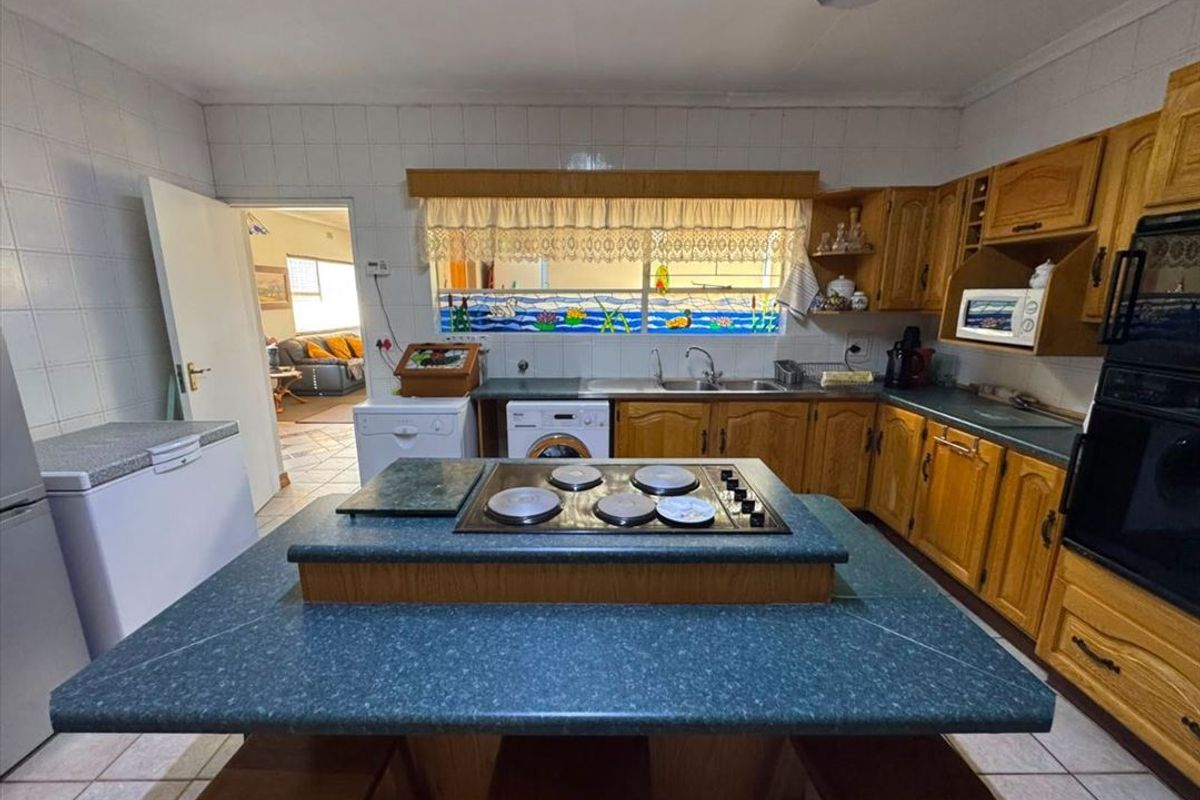 A functional kitchen featuring wooden cabinetry, a central island with an integrated electric hob, built-in oven, and tiled finishes throughout.