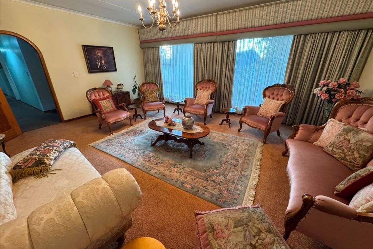 A traditional living room featuring an arched doorway, a central chandelier, and floor-to-ceiling window treatments with a built-in pelmet.