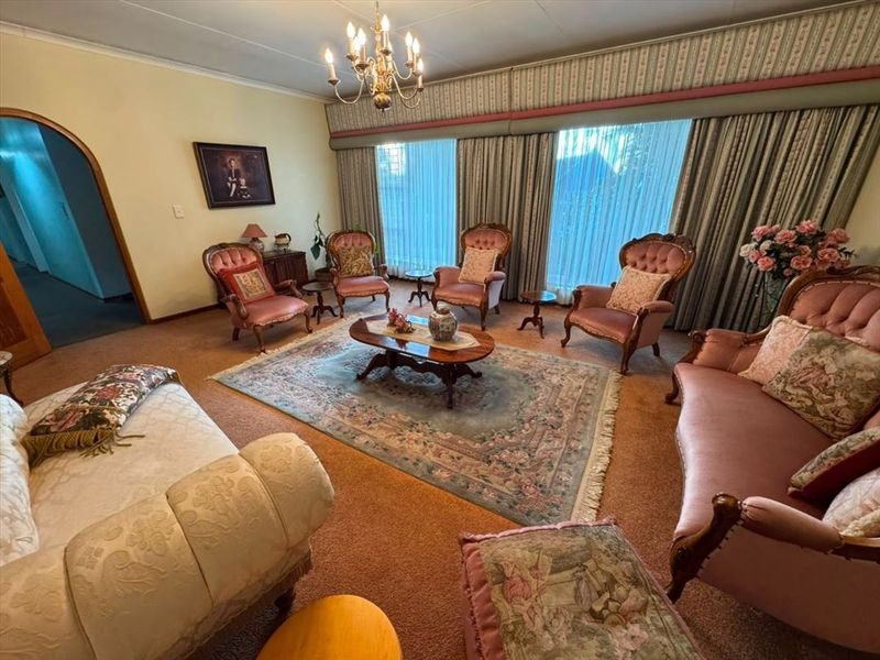 A traditional living room featuring an arched doorway, a central chandelier, and floor-to-ceiling window treatments with a built-in pelmet.