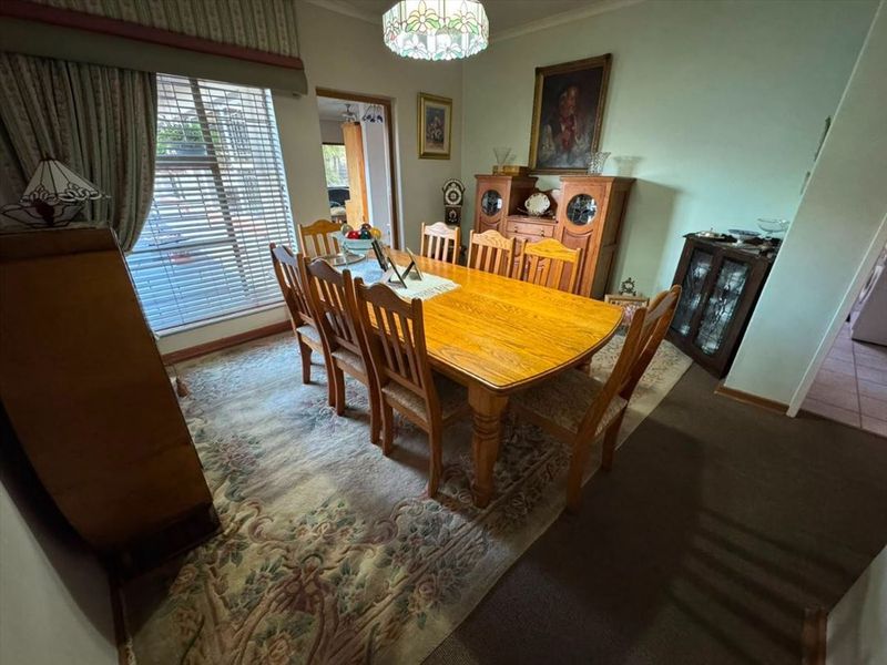 A traditional dining room featuring carpeted flooring, venetian blinds, and a decorative ceiling light fixture, offering a functional space for family meals.