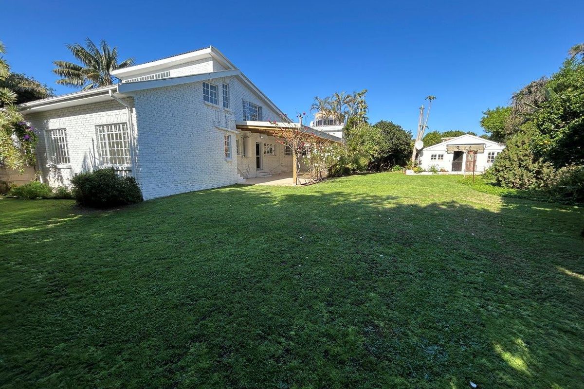 Spacious rear garden featuring a well-maintained lawn, a painted brick house exterior with a covered patio, and a separate outbuilding.