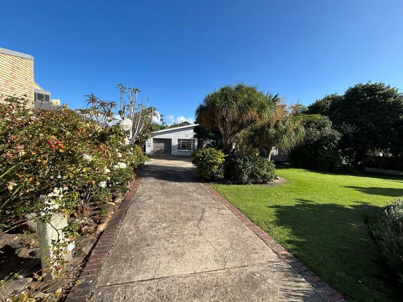 Front view of the property featuring a concrete driveway with brick edging, established garden landscaping, and a single garage door.