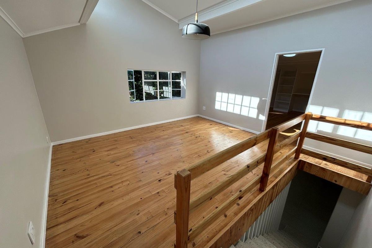 An open-plan living area featuring polished timber flooring, a vaulted ceiling with a skylight, and a timber balustrade overlooking the staircase.