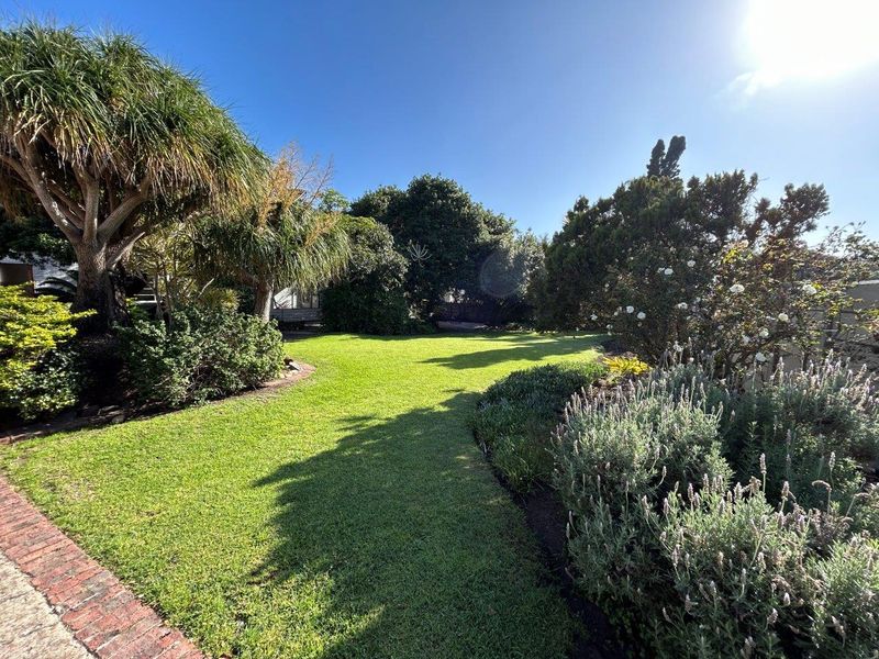 A well-maintained garden featuring a lush green lawn, mature trees, and established shrubbery with brick border detailing.