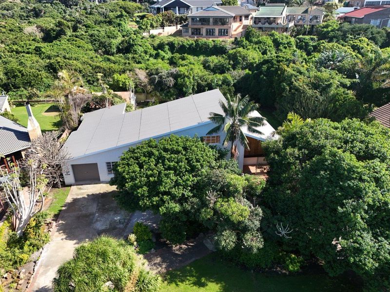 Aerial view of the property showcasing the metal roof, attached garage, driveway, and surrounding lush garden landscape.