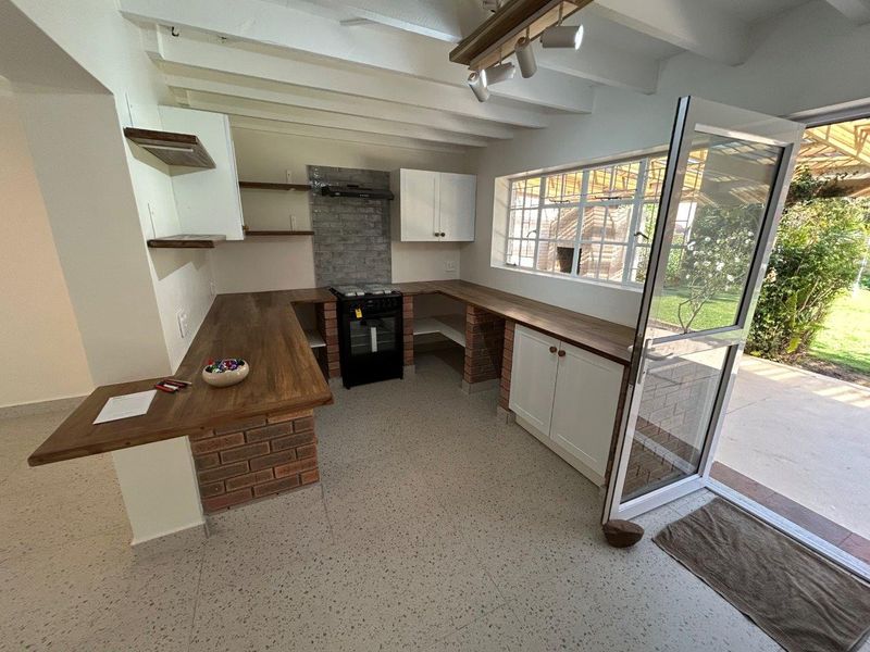 A bright, modern kitchen featuring exposed brick cabinetry bases, wooden countertops, a freestanding oven, and direct access to the garden through an aluminium door.