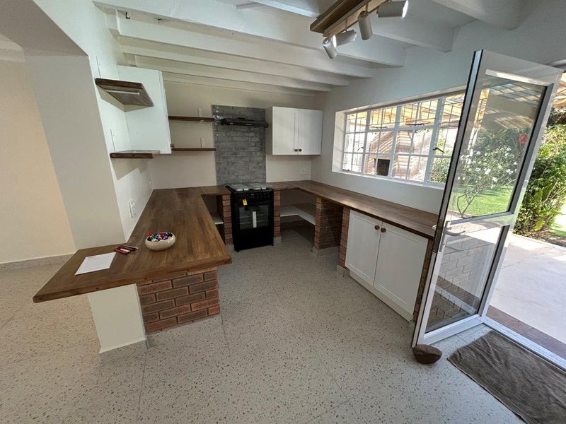A bright kitchen featuring exposed brick cabinetry, wooden countertops, terrazzo flooring, and an exposed beam ceiling with direct access to the garden.