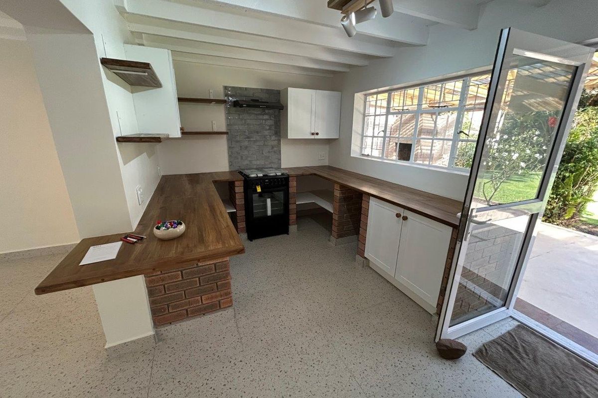 A bright kitchen featuring exposed brick cabinetry, wooden countertops, terrazzo flooring, and an exposed beam ceiling with direct access to the garden.