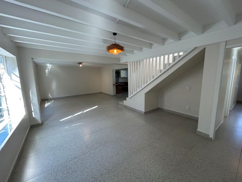 Spacious open-plan living area featuring exposed beam ceilings, terrazzo flooring, and a staircase with a white balustrade.