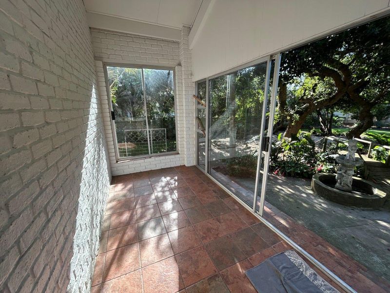 A covered patio area featuring tiled flooring, painted brick walls, and large sliding glass doors that provide access to the garden.