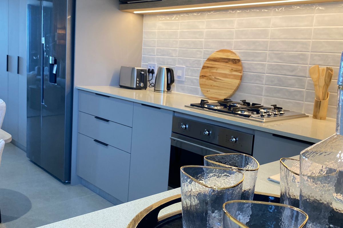 Modern kitchen featuring sleek grey cabinetry, stone countertops, subway tile backsplash, and integrated gas hob with built-in oven.