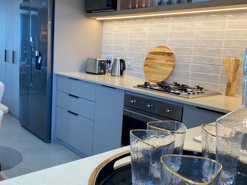 Modern kitchen featuring sleek grey cabinetry, stone countertops, subway tile backsplash, and integrated gas hob with built-in oven.