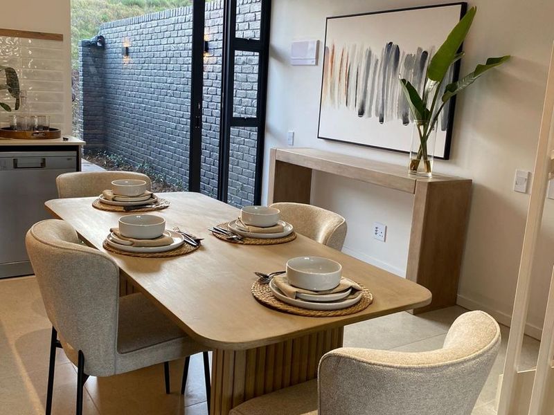 Modern open-plan dining area featuring tiled floors, recessed lighting, and seamless access to an outdoor patio through a black aluminium framed glass door.