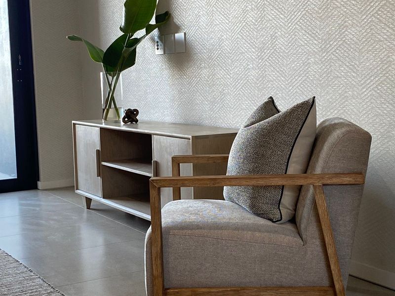 A modern living area featuring neutral textured wallpaper, large format floor tiles, and a sliding glass door providing natural light.