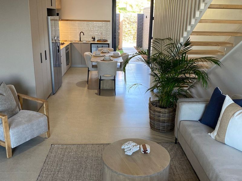 Modern open-plan living and kitchen area featuring sleek cabinetry, integrated appliances, tiled flooring, and a timber staircase with a contemporary slatted balustrade.