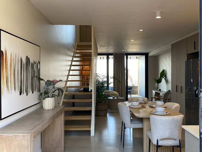 Modern open-plan living and dining area featuring tiled flooring, recessed lighting, and a timber staircase leading to the upper level.