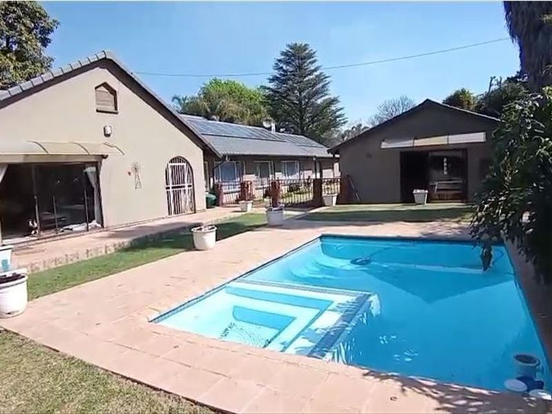 Rear view of the property featuring a swimming pool, paved pool deck, lawn area, and access to the main house and secondary structure.