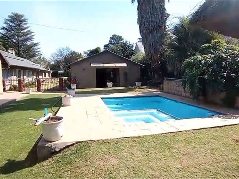 A backyard area featuring a swimming pool with a paved surround, adjacent lawn, and a detached garage structure.
