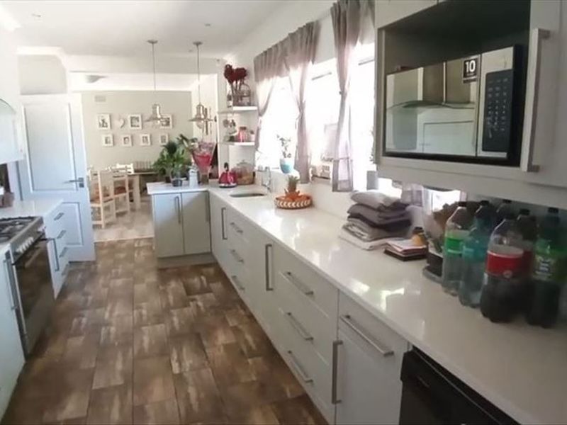 Open-plan kitchen featuring modern white cabinetry, quartz countertops, gas hob, and integrated microwave, flowing into a dining area with wood-look flooring.