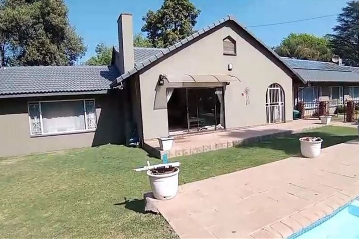 Rear view of the house featuring a tiled roof, paved patio area, swimming pool, and solar panels installed on the roof.