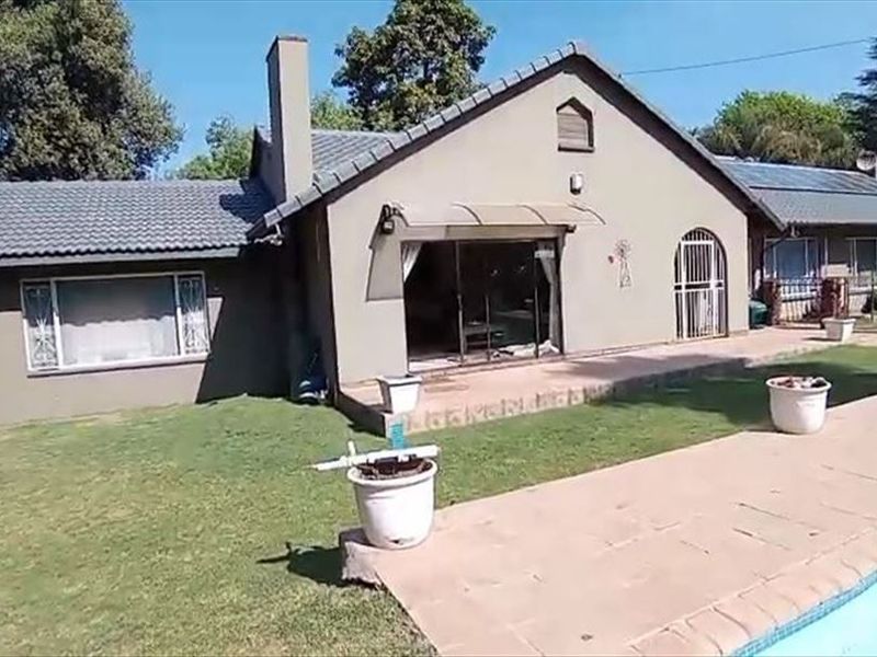 Rear view of the house featuring a tiled roof, paved patio area, swimming pool, and solar panels installed on the roof.