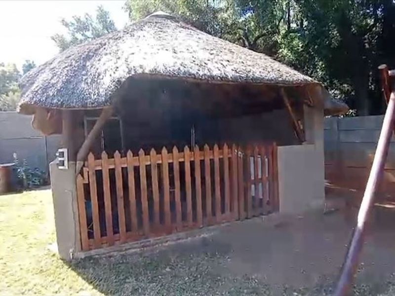 Outdoor thatched lapa area featuring a timber picket fence enclosure, situated in a garden setting.
