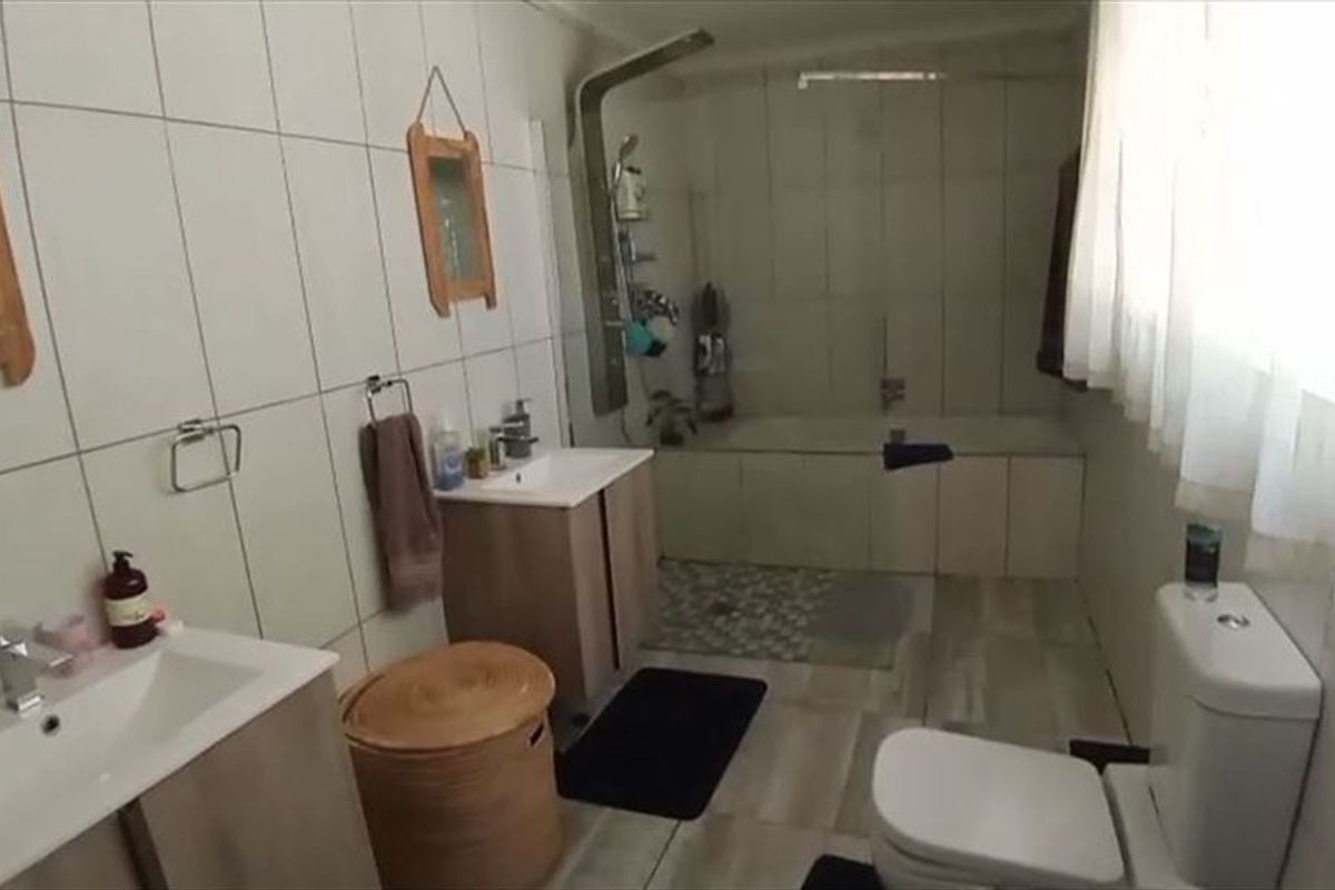 A functional bathroom featuring a dual vanity, a built-in bathtub with a shower panel, and tiled finishes throughout.