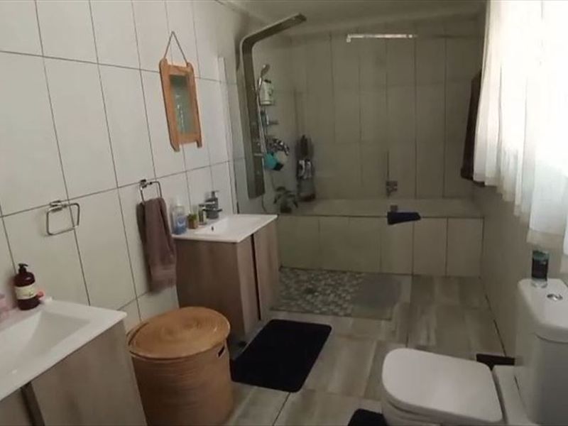 A functional bathroom featuring a dual vanity, a built-in bathtub with a shower panel, and tiled finishes throughout.
