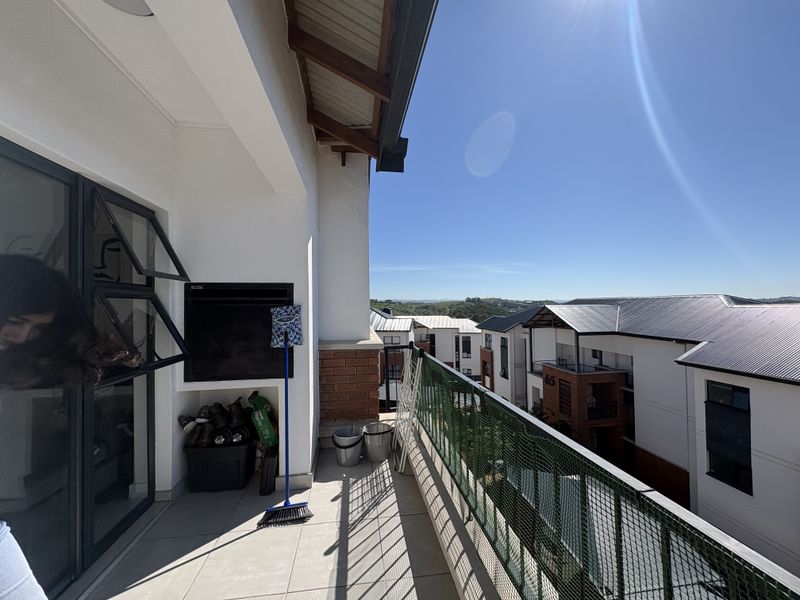 A spacious balcony featuring a built-in braai, tiled flooring, and a metal balustrade, offering an elevated view of the surrounding residential complex.