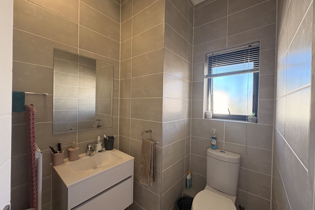 A modern, well-maintained bathroom featuring floor-to-ceiling wall tiles, a wall-mounted vanity with a basin, and a toilet.
