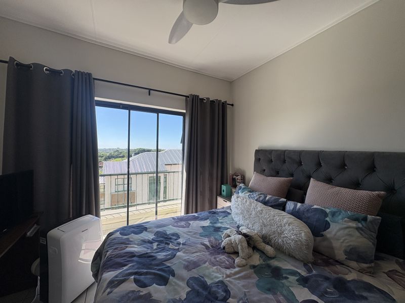 A well-lit bedroom featuring a ceiling fan and a sliding glass door that provides access to a balcony with an outdoor view.