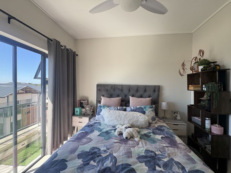 A well-lit bedroom featuring a ceiling fan and a large sliding glass door providing access to an outdoor balcony area.