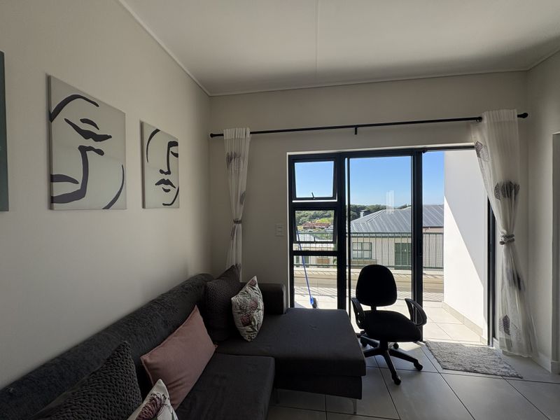 A bright living room featuring tiled flooring and a large sliding glass door that provides access to an outdoor balcony area.