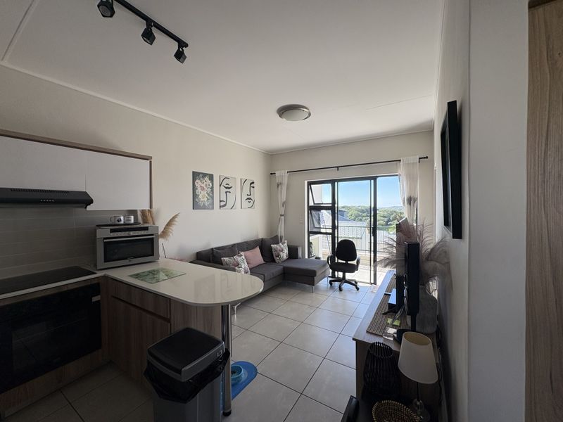 Open-plan living area featuring a modern kitchen with built-in appliances, breakfast counter, tiled floors, and direct access to a balcony with scenic views.