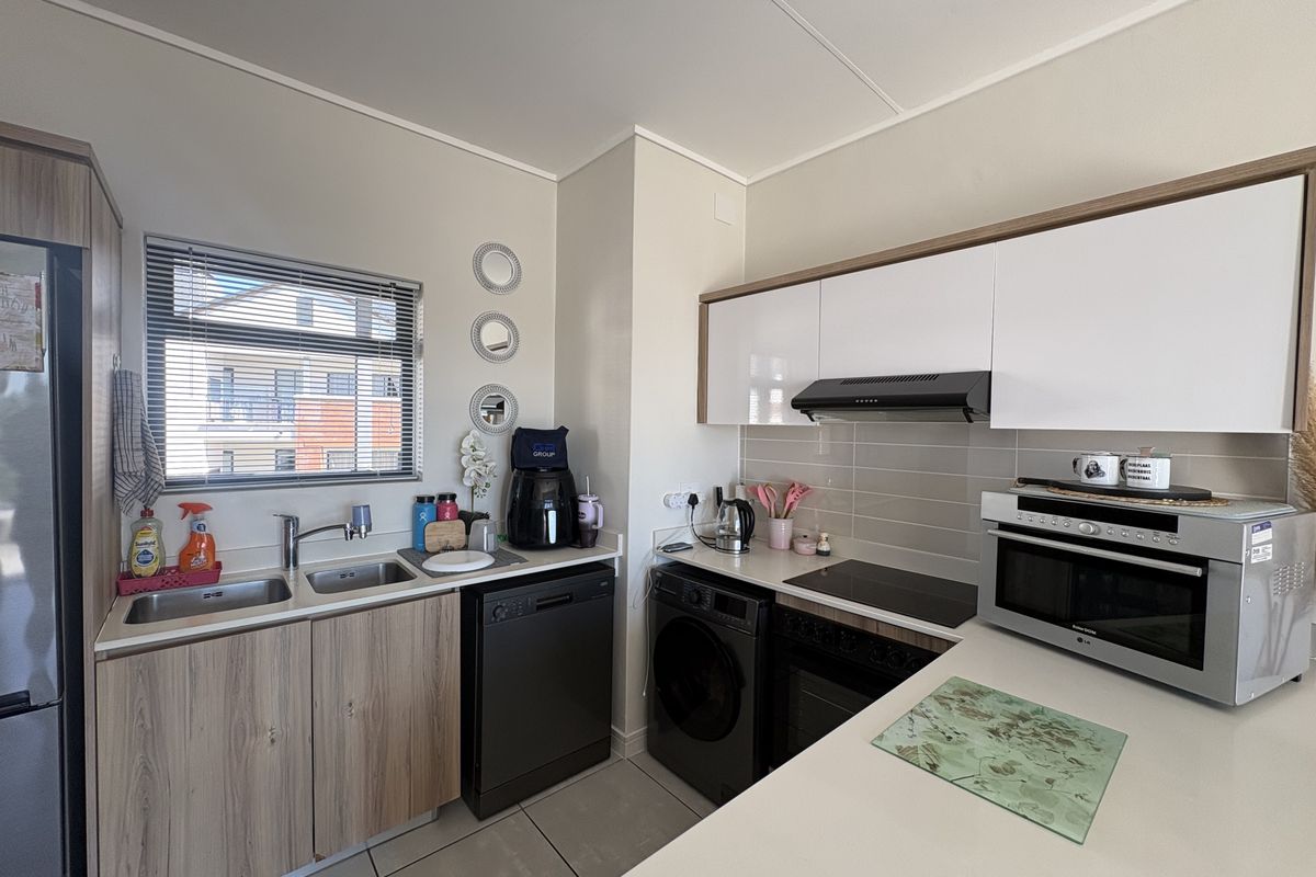 Modern kitchen featuring sleek white and wood-grain cabinetry, integrated appliances, a double sink, and a tiled splashback with ample counter space.