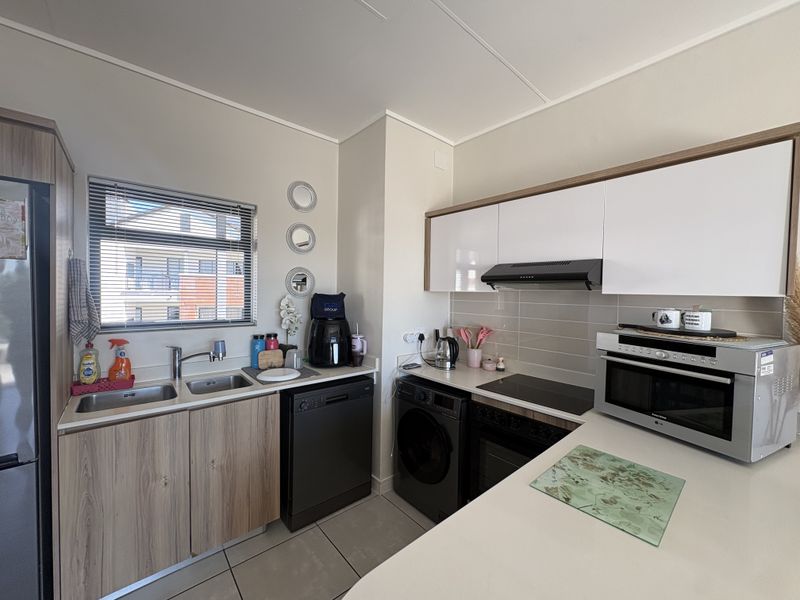Modern kitchen featuring sleek white and wood-grain cabinetry, integrated appliances, a double sink, and a tiled splashback with ample counter space.