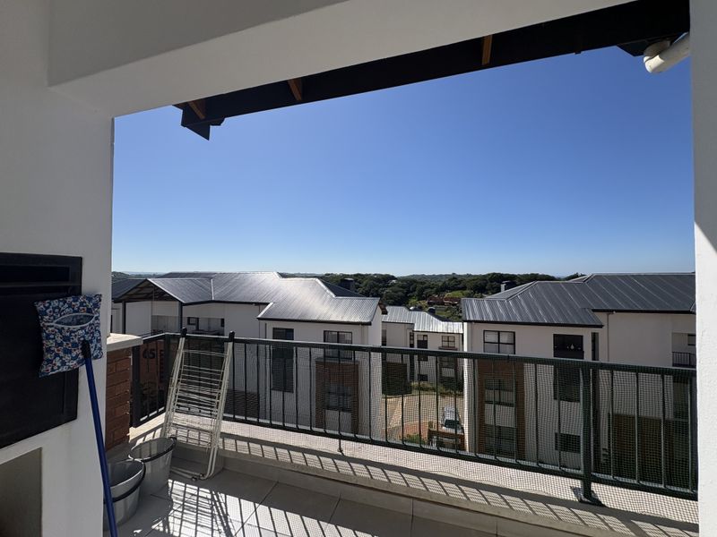 A covered balcony featuring tiled flooring, a built-in braai, and a metal balustrade, offering an elevated view of the surrounding residential complex.