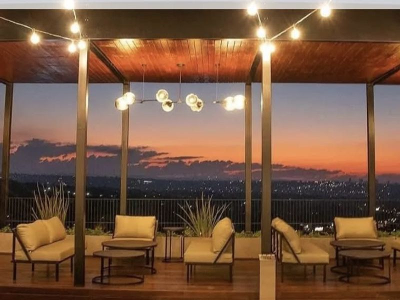 A spacious covered balcony featuring timber decking and ceiling, metal structural supports, and a built-in planter, offering expansive sunset views.
