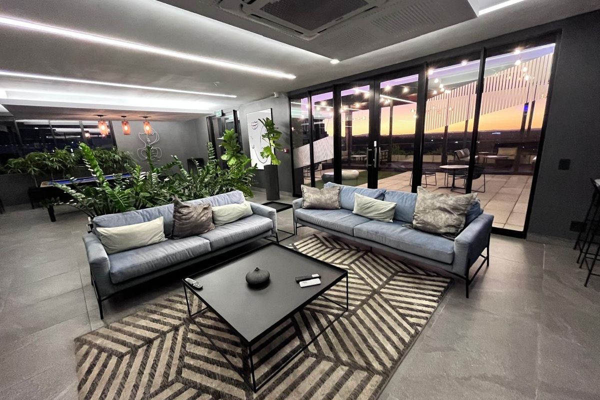 Modern, well-lit living area featuring large glass sliding doors leading to an outdoor patio, recessed ceiling lighting, and ducted air conditioning.
