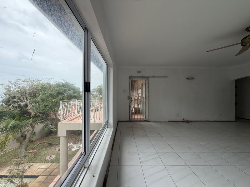 Spacious, empty living area featuring large windows with garden views, tiled flooring, and a security gate leading to an outdoor space.