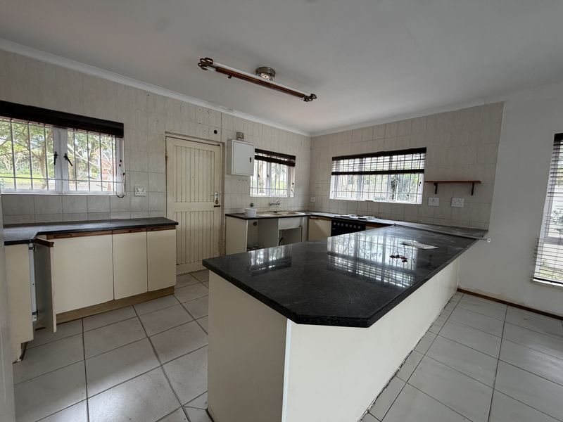 A spacious, empty kitchen featuring granite countertops, tiled flooring, and ample cabinetry, offering a blank canvas for renovation and modernization.